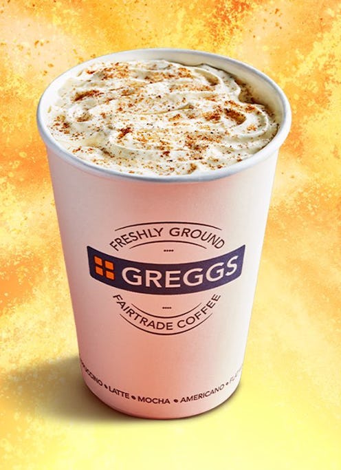 A greggs paper cup against an orange and yellow swirled background. The cup is filled with creamy fo...