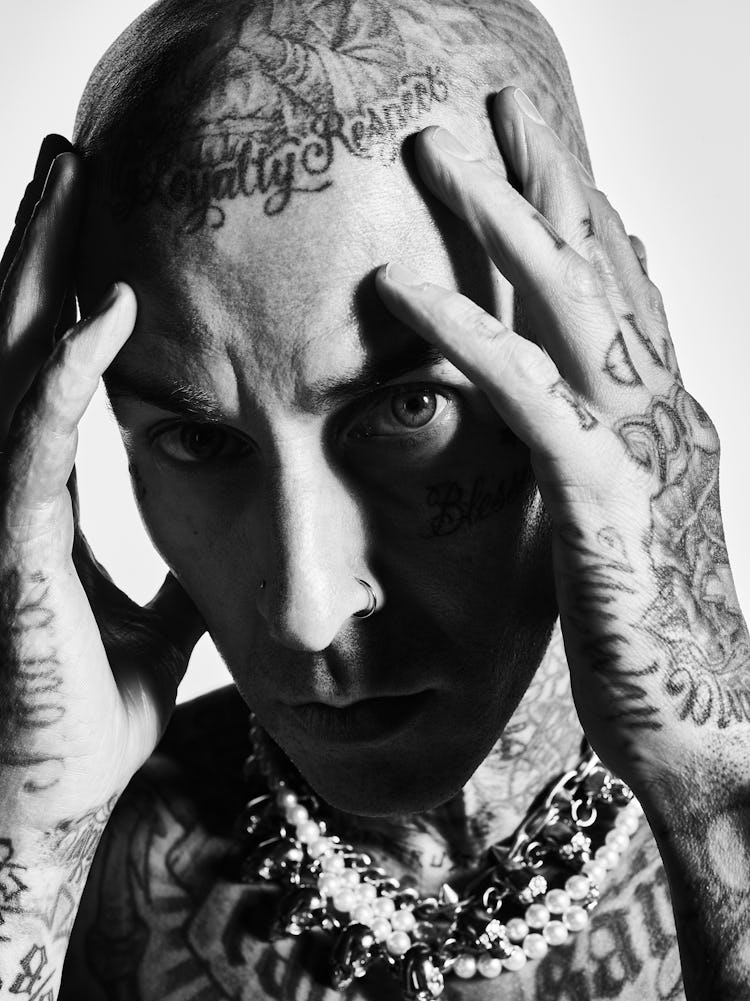 A black and white close-up image of Travis Barker with his hands on his head.