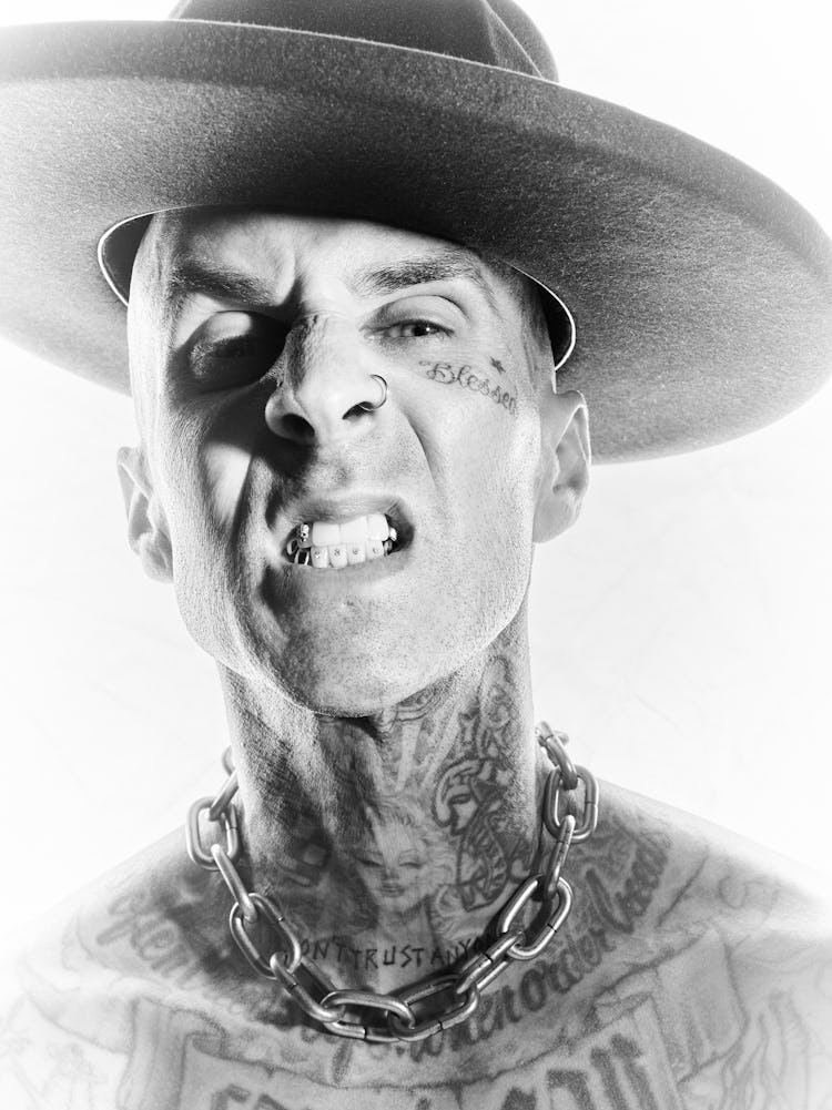 NYLON cover star Travis Barker shows his teeth while wearing a wide-brimmed hat and posing for a clo...