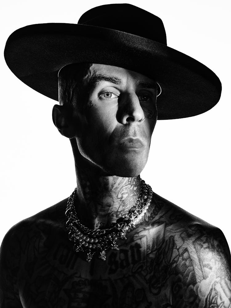 A close-up portrait of NYLON cover star Travis Barker in black and white wearing a black wide-brimme...