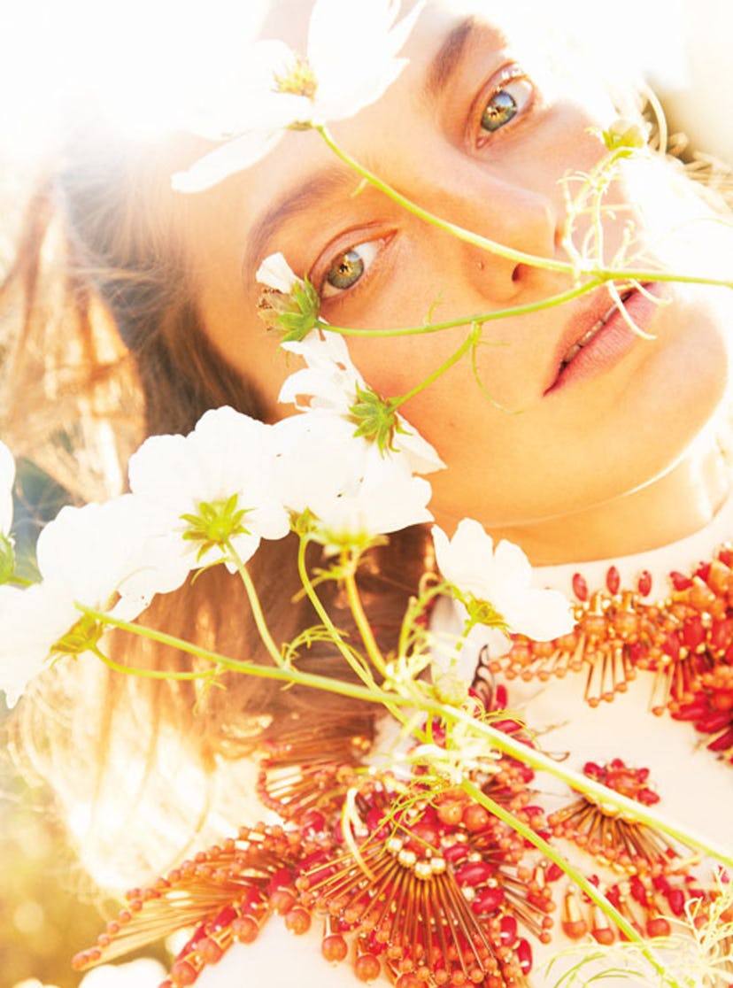 A woman lying in a field with flowers in front of her face on a bright sunny summer day