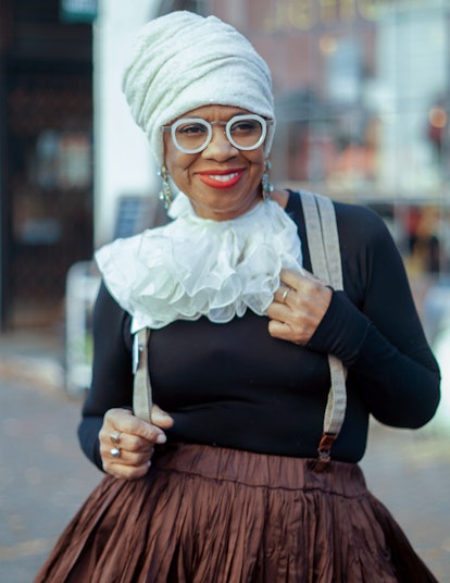 Arlinda McIntosh in a black shirt with white frills, a bronze satin skirt, a white headscarf and whi...