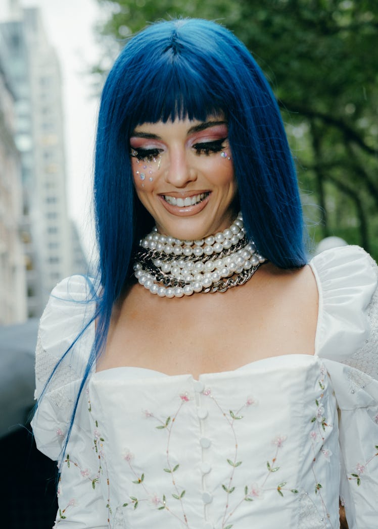 Woman wears blue hair and lots of pearl necklaces.