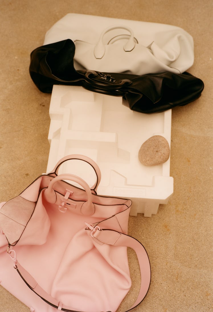 A pink, a white, and a black Salvatore Ferragamo bag laid out next to a white sculpture
