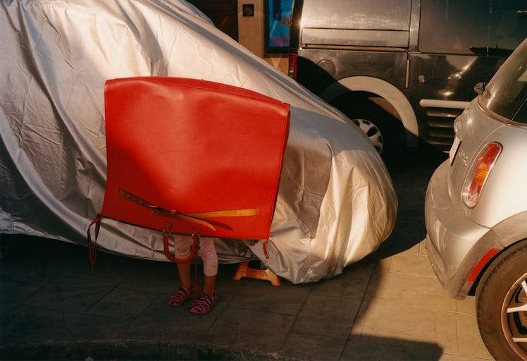 A red Marni bag over a person's head who is standing on a parking lot