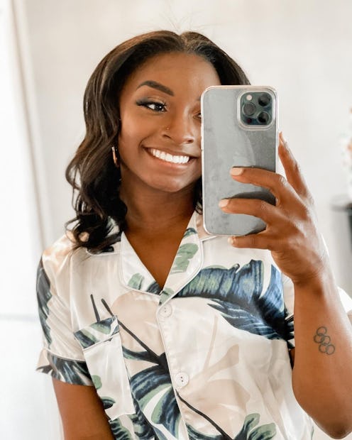 Simone Biles with curled hair taking mirror selfie and smiling