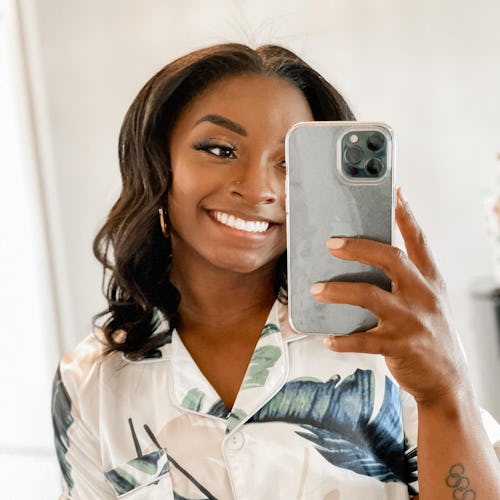 Simone Biles with curled hair taking mirror selfie and smiling 