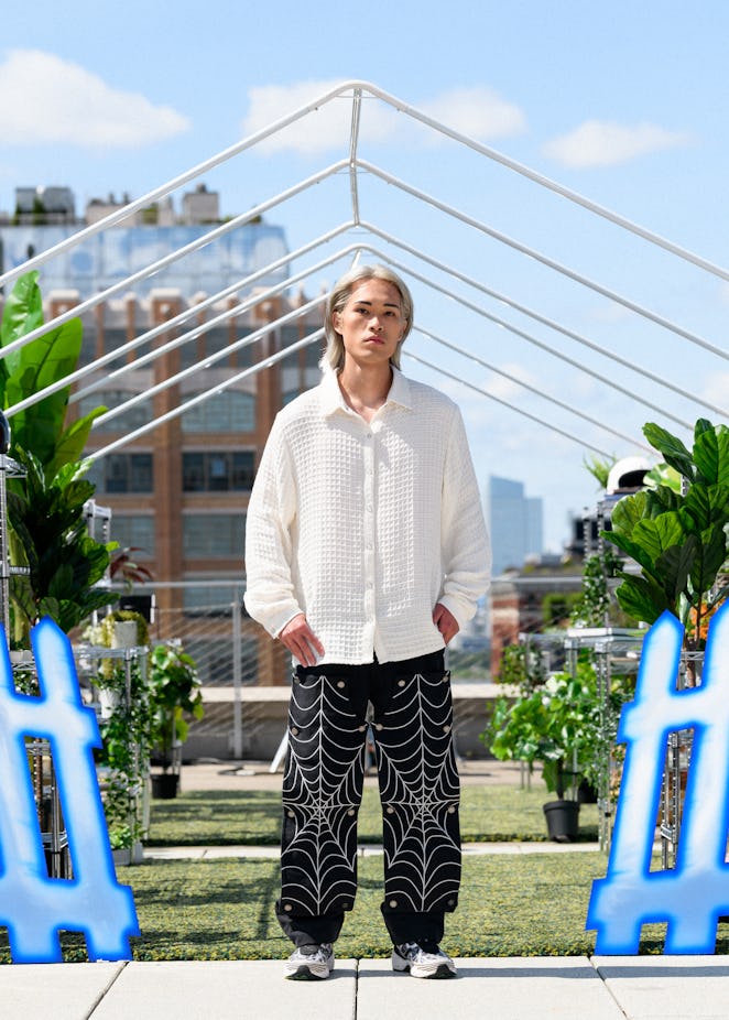 A model in a piece from Tombogo's "Nature Is Healing": white button-up and black cargo pants with wh...