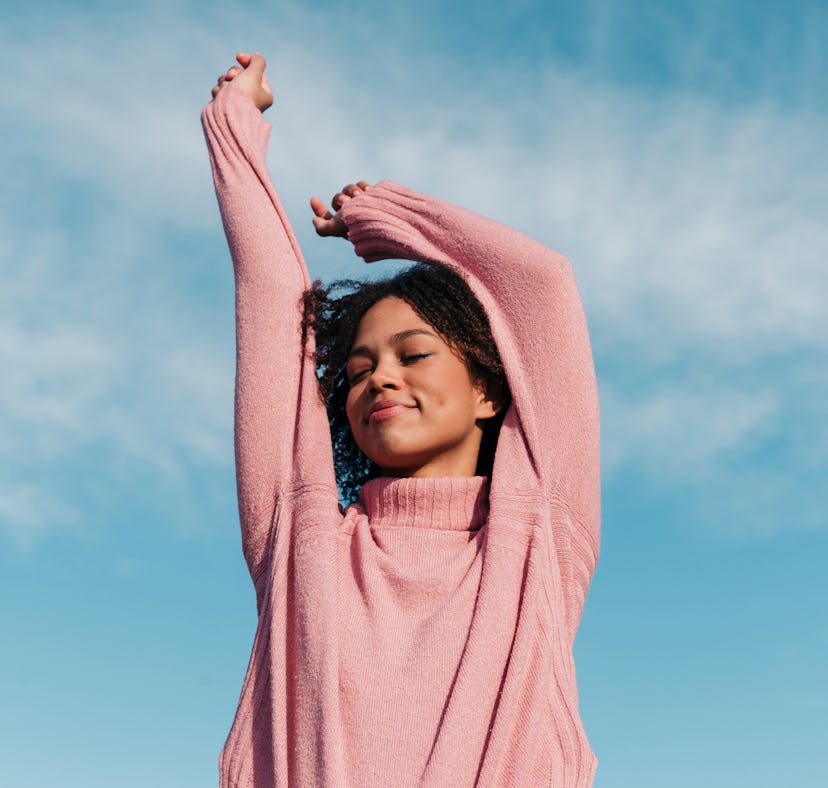 Smiling young woman in a pink sweater, having the best week of September 20, 2021, per her zodiac si...