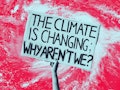A hand holding a sign with the text "The climate is changing, why aren't we?"