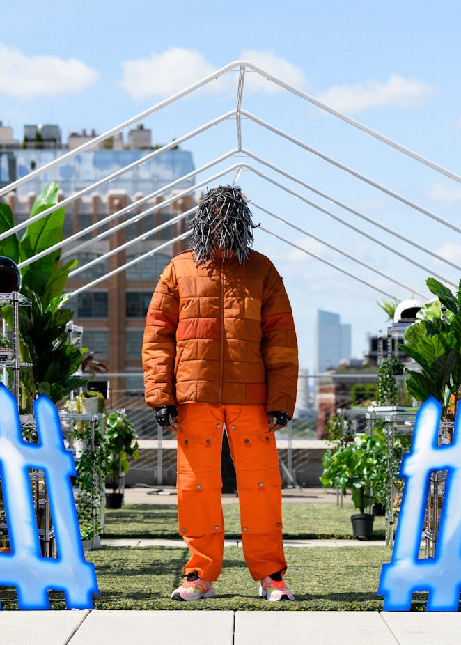 A model in a piece from Tombogo's "Nature Is Healing": a copper puffer jacket and orange cargo pants...