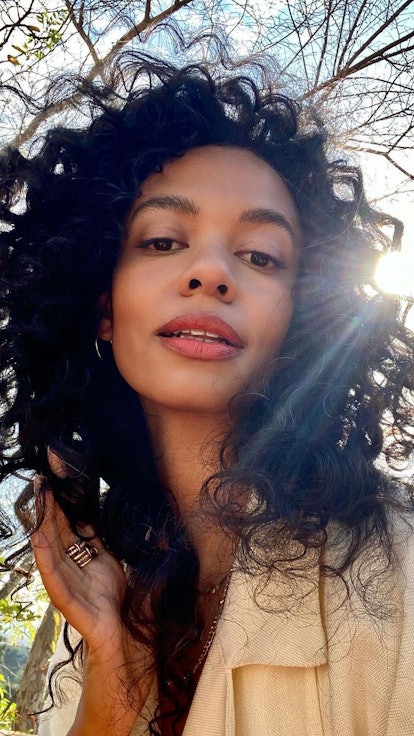 Aurora James with minimalist makeup for fall taking a selfie with trees in her background