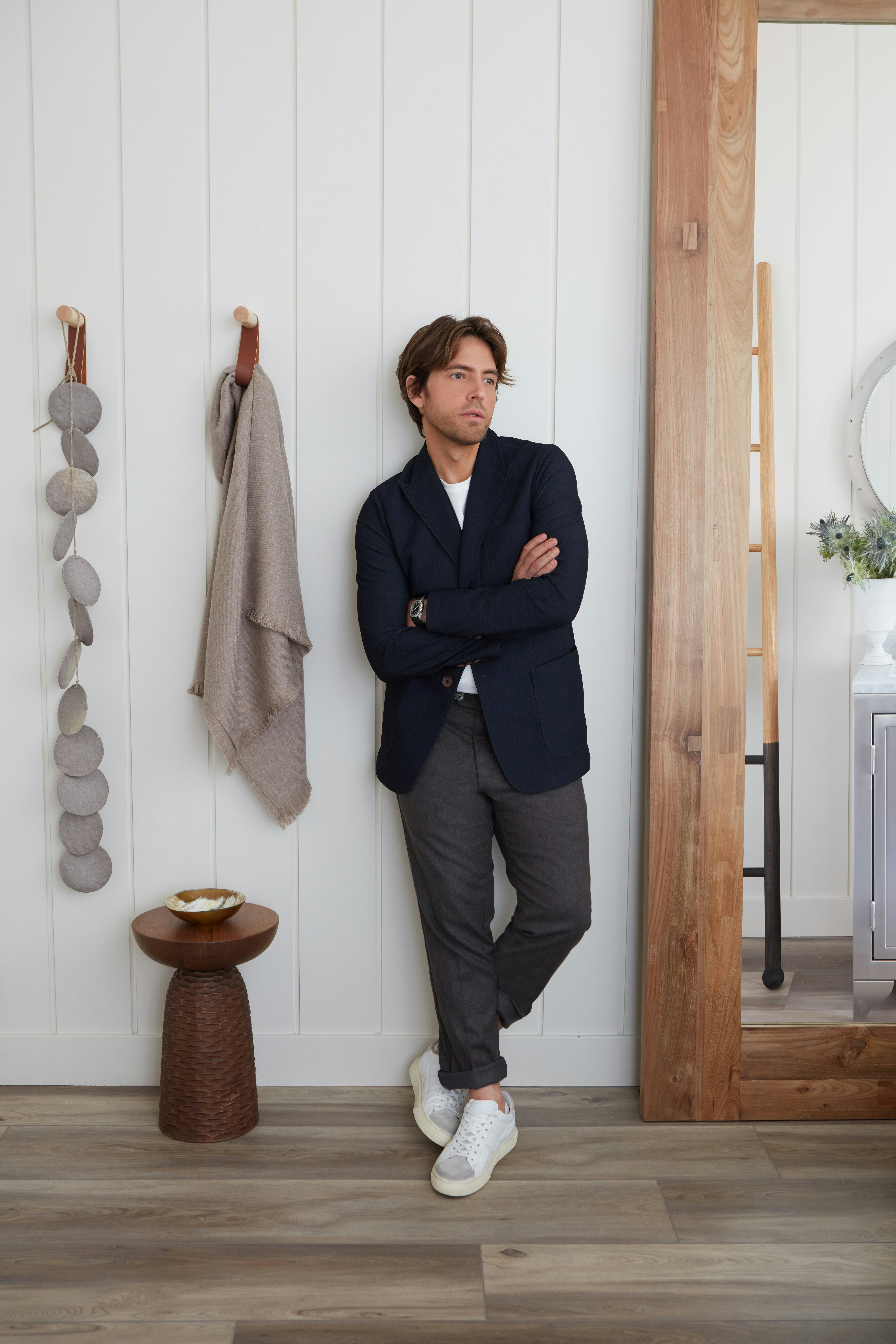 Ivan Pol in a navy blazer, white shirt and grey trousers leaning against a wall