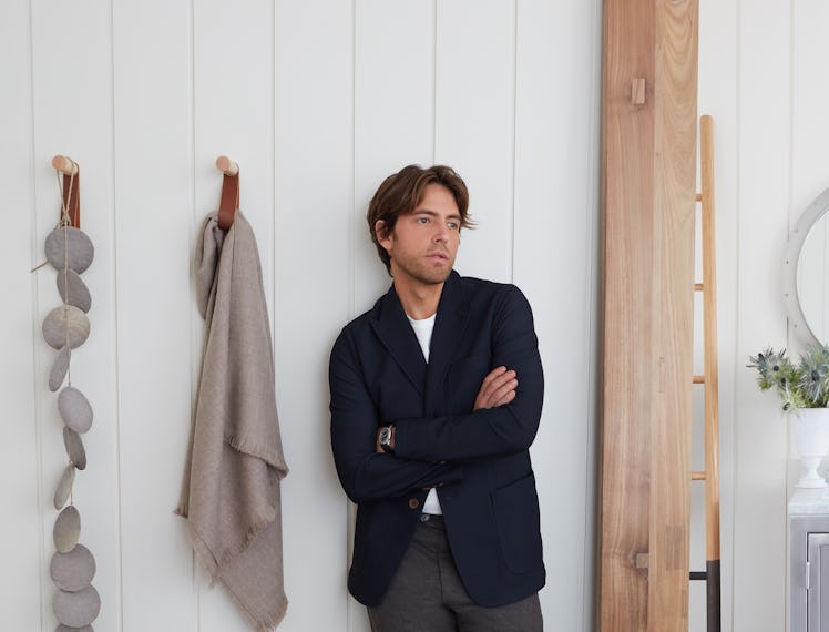 Ivan Pol in a navy blazer, white shirt and grey trousers leaning against a wall