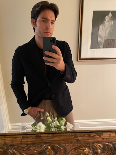 Ivan Pol in a black shirt and camel trousers taking a selfie in a mirror