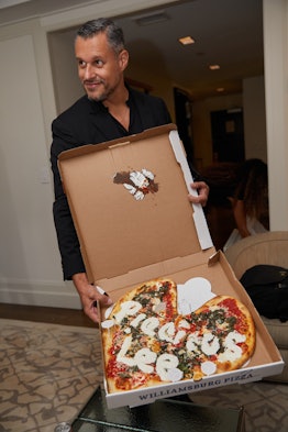 A man holding a heart-shaped pizza with "Precious Lee" cheese text sign