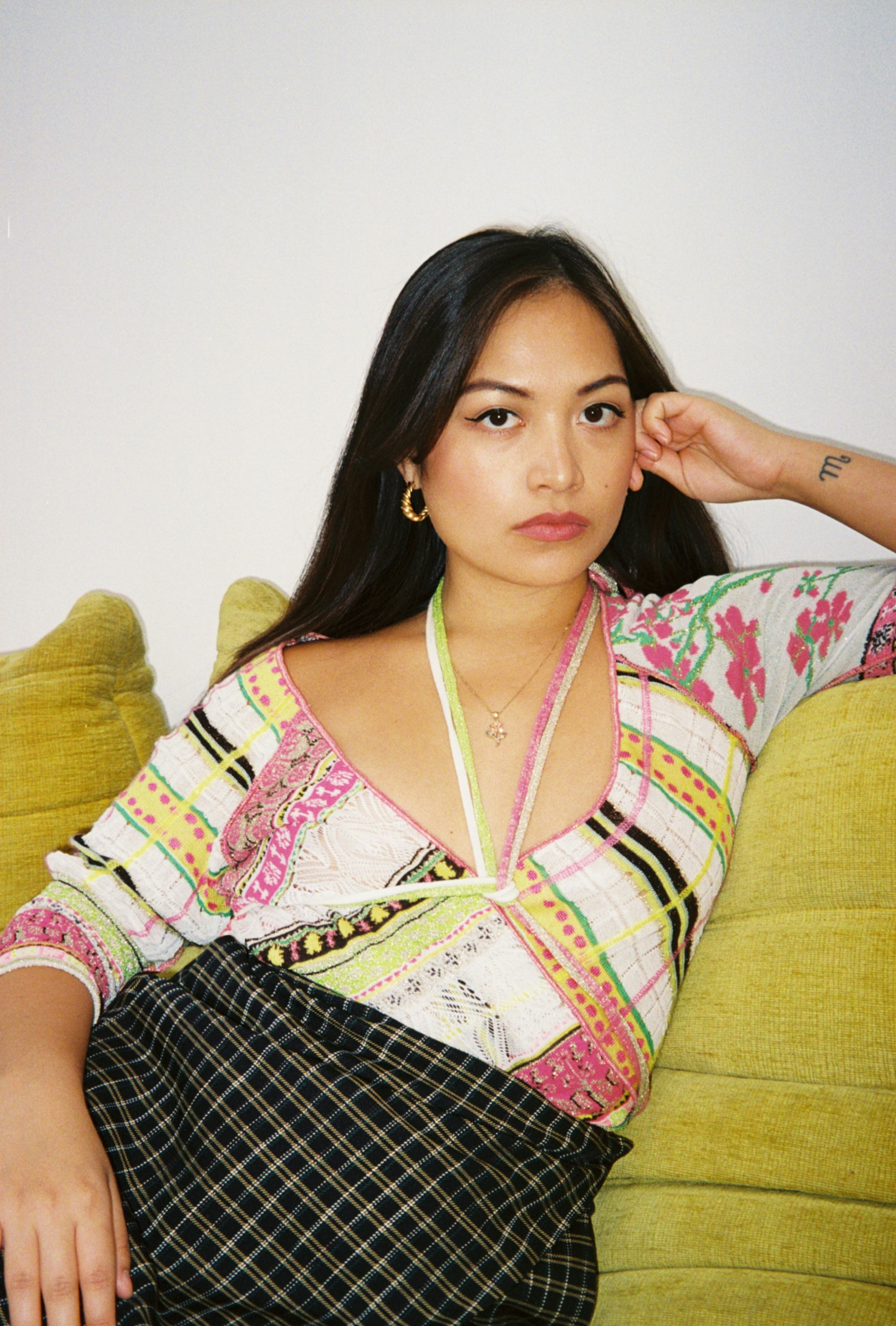 Marlow Granados sitting on a yellow couch while wearing a striped pink and yellow shirt
