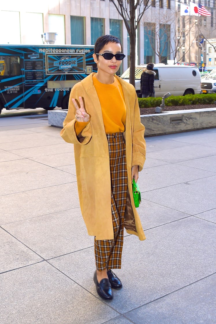 Zoe Kravitz in a yellow coat. orange sweater, plaid pants and black leather loafers in the street 