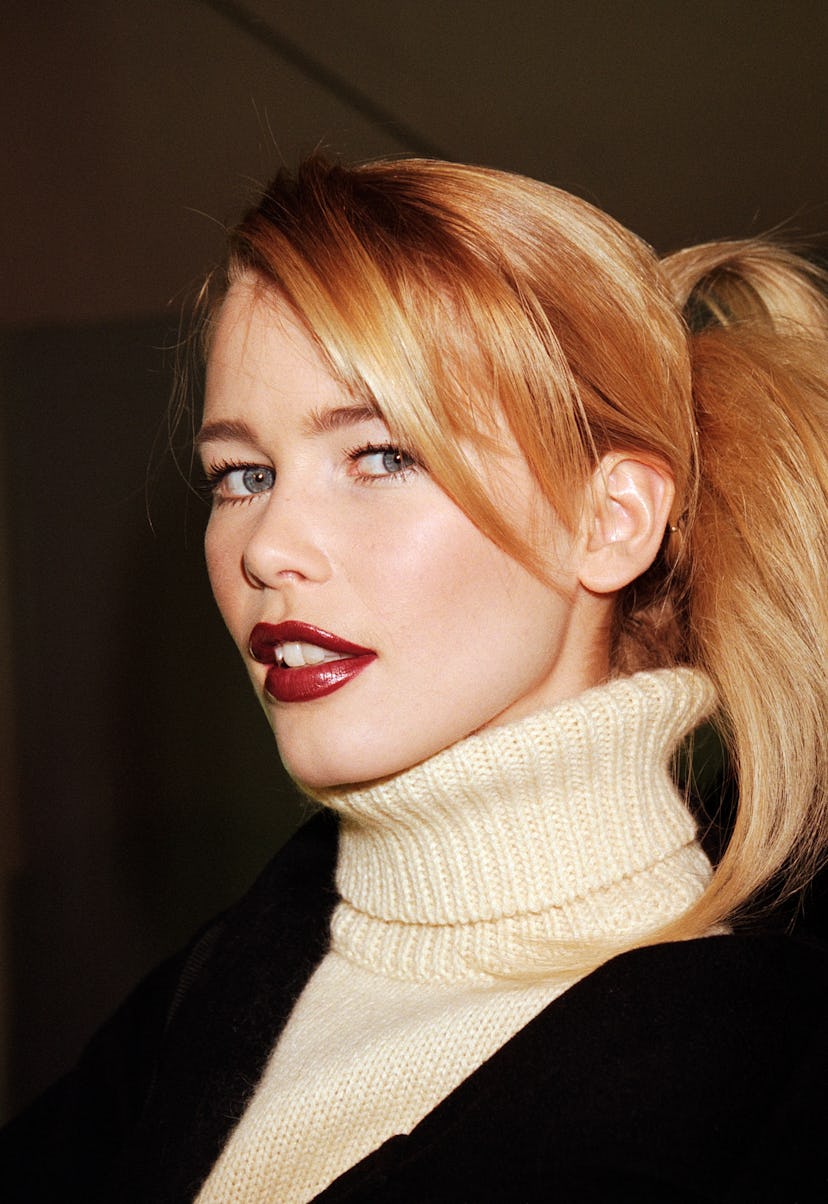A portrait of Claudia Schiffer with an updo hairstyle in a white knit turtleneck and a black blazer