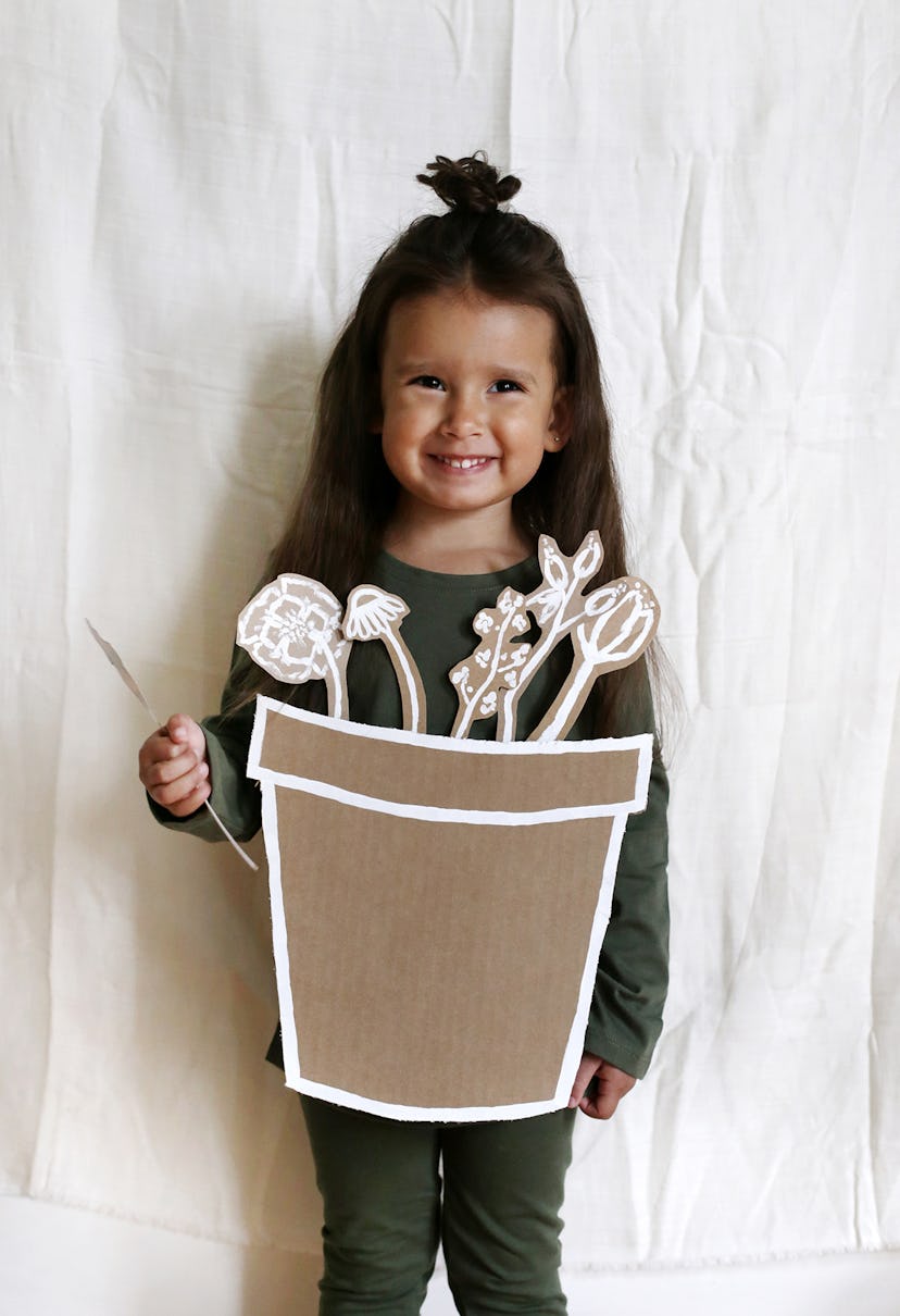 Little girl in green, wearing flower pot made from cardboard 