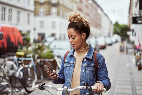 Woman standing with her bike looking at her phone.