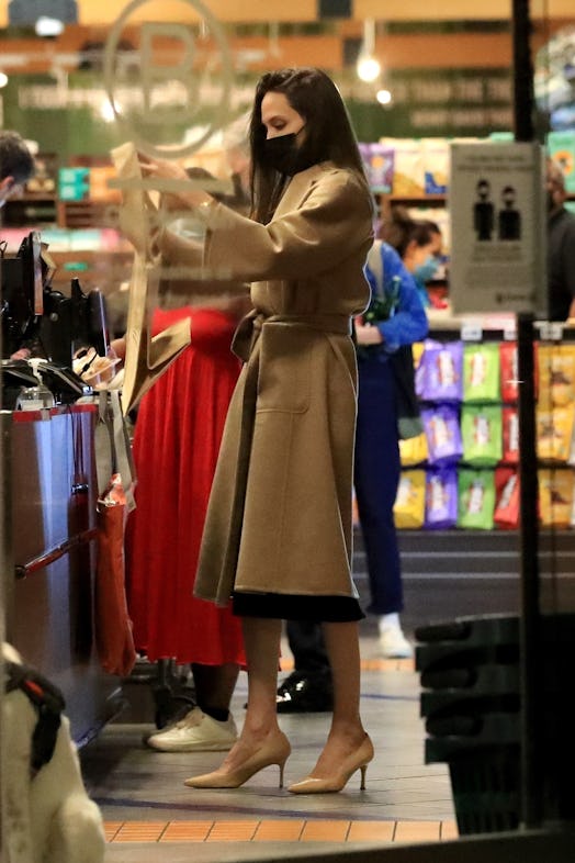 Angelina Jolie wears a trench coat, black dress, and nude heels when grocery shopping.