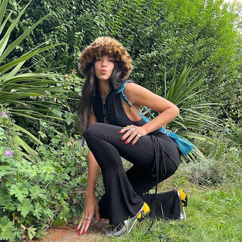 Dua Lipa poses in black flared trousers, a halter tank, and a fuzzy cheetah bucket hat.