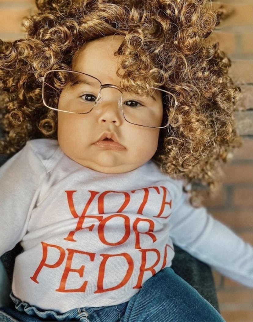 baby dressed as Napoleon Dynamite for Halloween- curly wig, glasses, and "Vote For Pedro" Tshirt