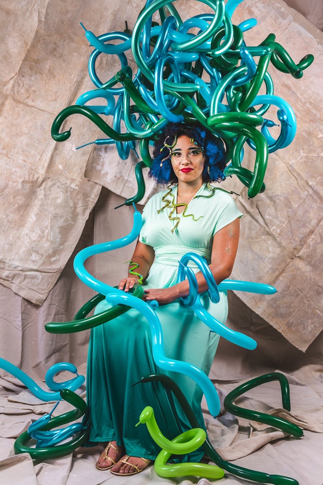 Woman sitting in chair dressed as Medusa with long balloons as snakes