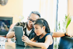 Child working on tablet with help of her dad