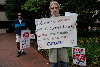 A white woman holds up a sign that says, "Educated parents are a school boards [sic] worst nightmare...