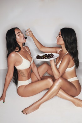 Kourtney Kardashian and Megan Fox pose for a SKIMS ad in white underwear while feeding each other ch...