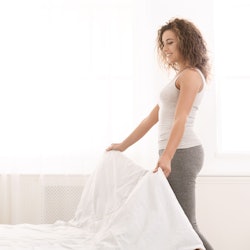 woman putting white sheets on bed
