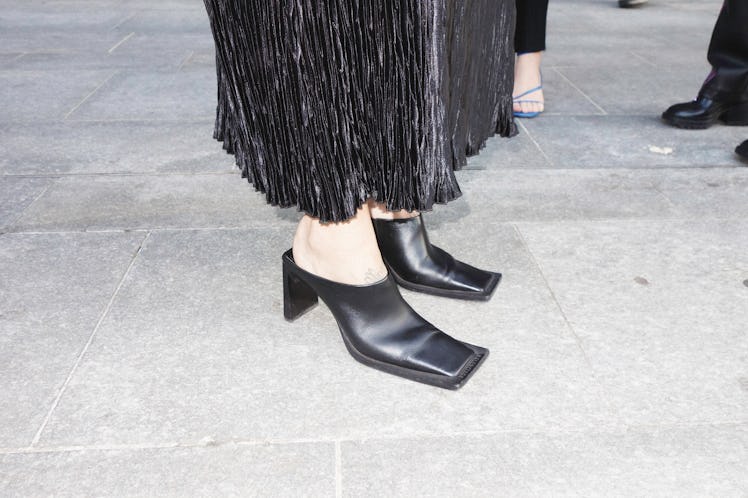 A close-up of a woman's leather black heels and black dress at Milan Fashion Week 2022