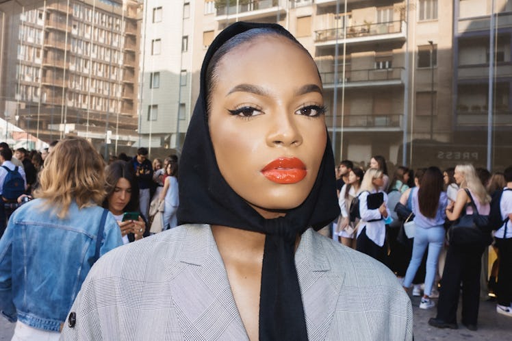 A woman in a grey blazer, and a black scarf on her head at Milan Fashion Week 2022