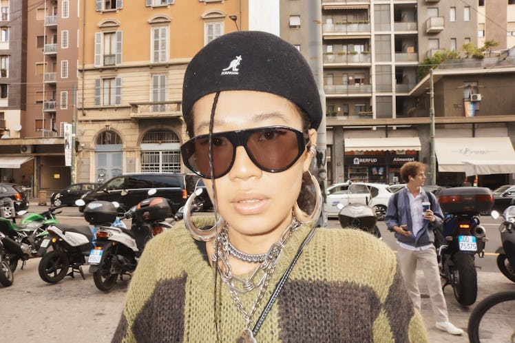 A woman in a beige-brown sweater and a black beret and sunglasses at Milan Fashion Week 2022