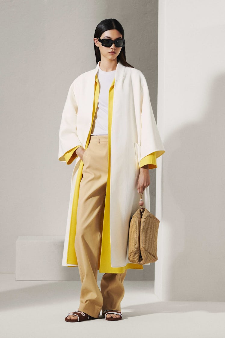 A model in a Loro Piana white and yellow coat, beige pants and sunglasses 