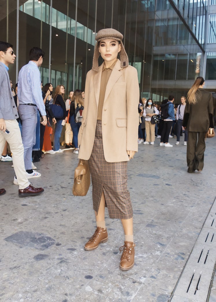 A woman in a beige shirt and blazer, brown checked skirt and hat at Milan Fashion Week 2022