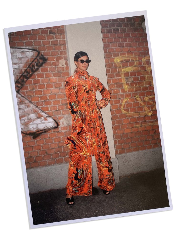 A woman in an orange-black swirl patterned dress, trousers and bag at Milan Fashion Week 2022