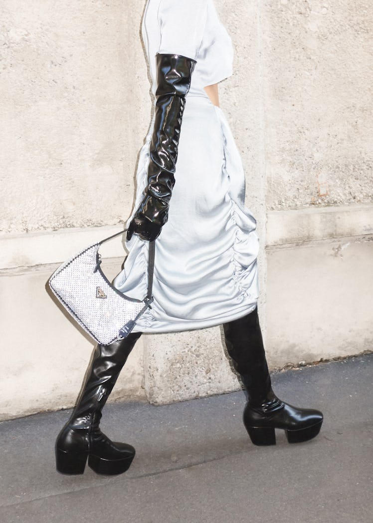 A model in a white dress, black gloves, shimmer bag and black boots at the Milan Fashion Week 2022