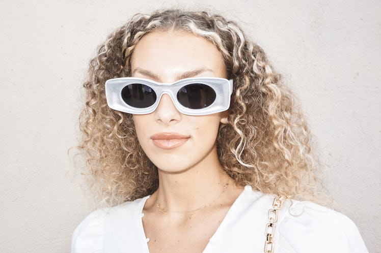 A curly-haired woman in a white top and black-white sunglasses at Milan Fashion Week 2022