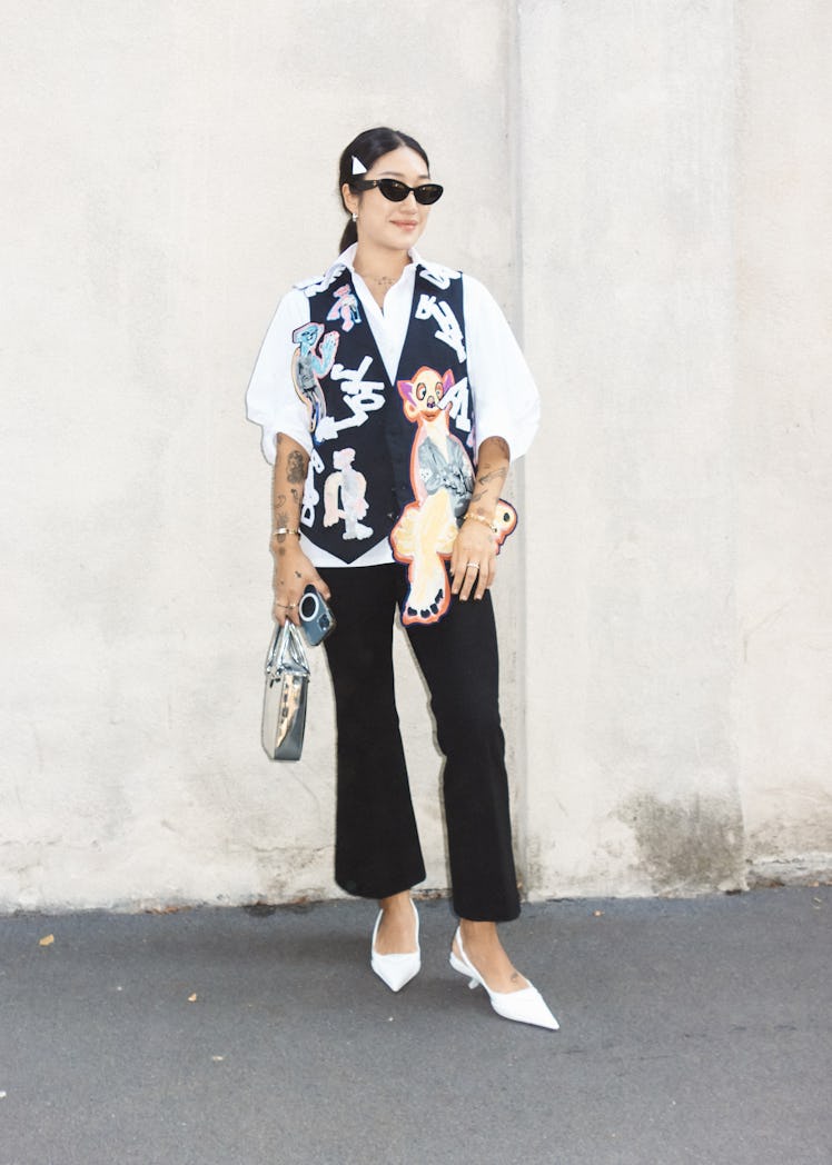 A woman in a white shirt, a black waistcoat with white patches and black trousers at Milan Fashion W...