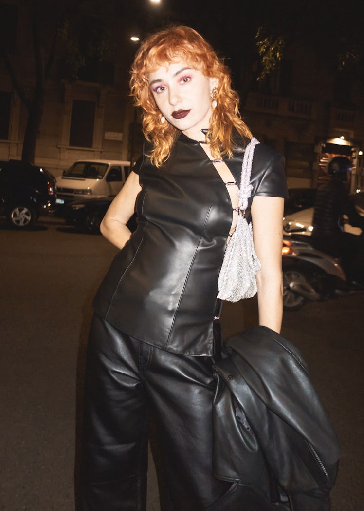 A woman in a black leather dress and a small shimmer bag at Milan Fashion Week 2022