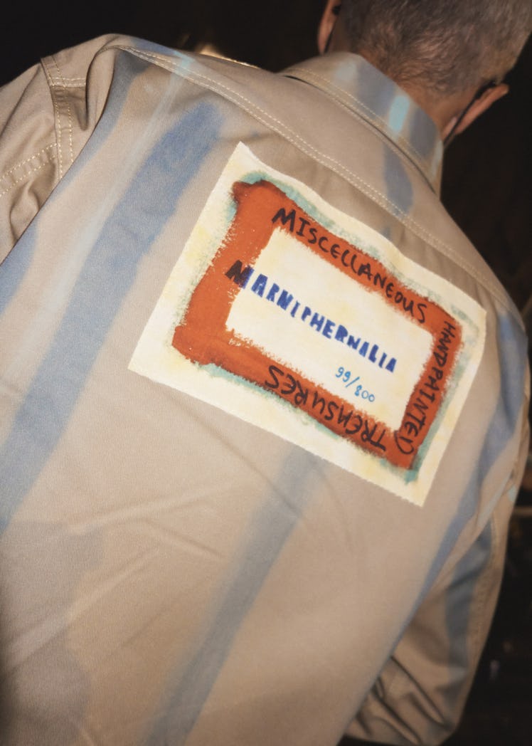The back of a man in a blue-white shirt with the text 'Miscellaneous Marniphernalia' 