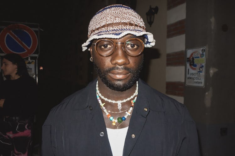 A man in a white top, black shirt and a knit bucket hat