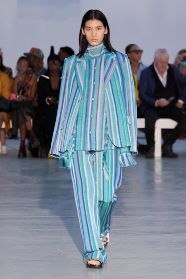 A model walking in a blue striped suit and shirt by Kenneth Ize on a runway