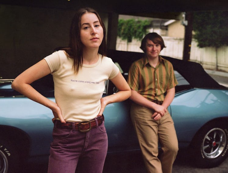 Alana Haim and Cooper Hoffman in front of a blue convertible in Licorice Pizza