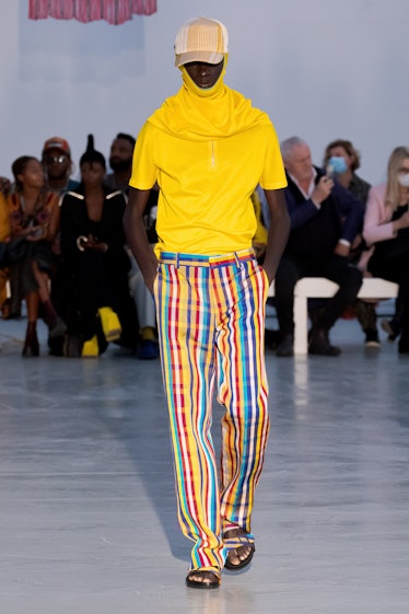 A model walking in  a yellow shirt and multi-colored pants by Kenneth Ize on a runway