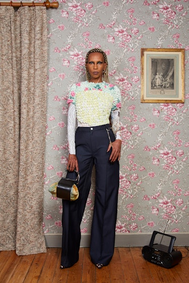 A model posing in a flora white-blue top and navy pants by Marine Serre in a room with pink floral w...