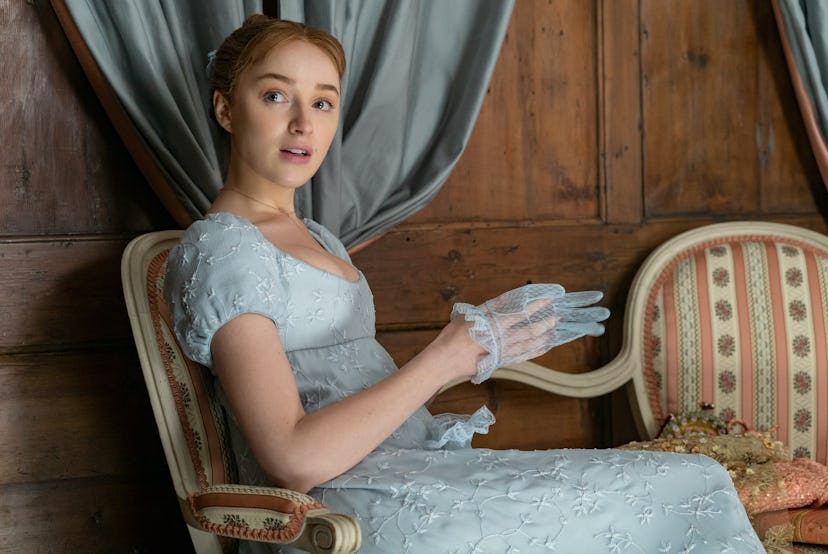 Daphne Bridgerton in a pale blue dress slipping a light blue glove onto her hand.